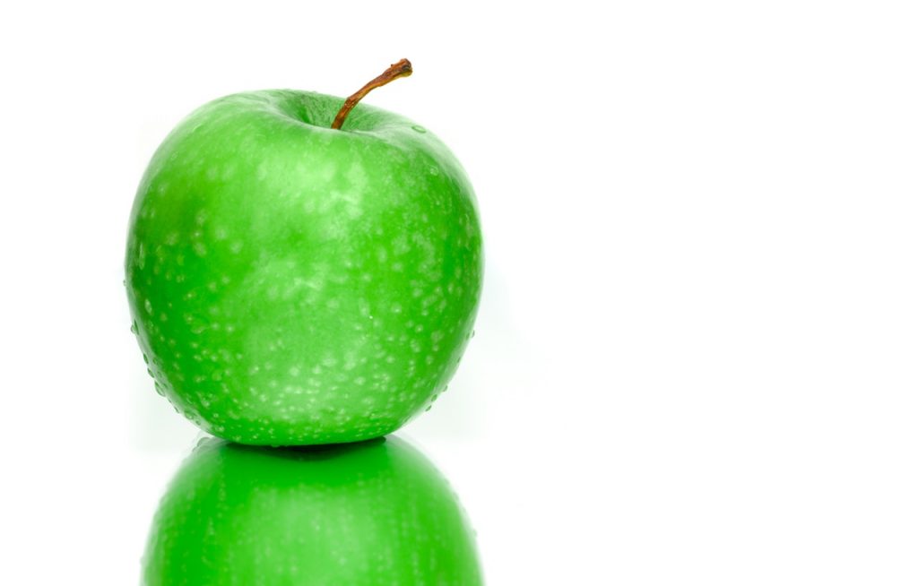 Green apple on reflective surface